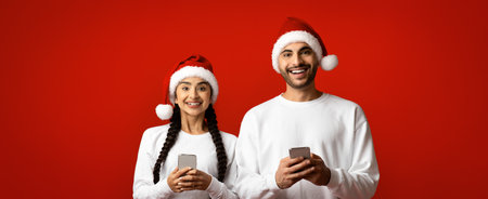 Cheerful Couple in Christmas Hats Using Phones Against Bright Red Background