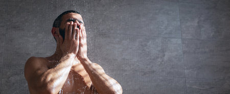 Man Washing His Face in the Shower While Water Flows Down a Tiled Wall