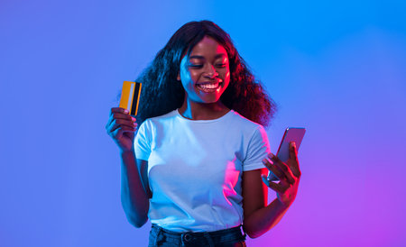 Woman Smiling While Using Smartphone and Holding Credit Card in Colorful Light