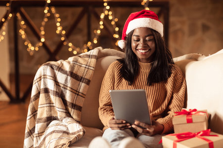 Woman in Christmas Hat Happily Using Tablet Near Holiday Gifts During Festive Seasonの写真素材