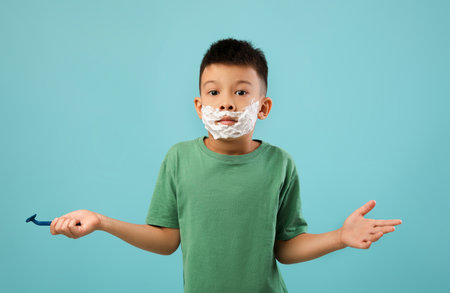 Young Boy With Shaving Cream on Face Looks Puzzled in Bright Blue Backgroundの写真素材