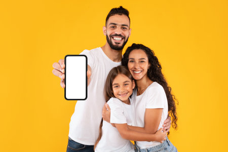 Happy Family Posing Together Against a Bright Yellow Background While Showcasing a Smartphone