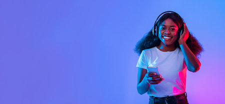 Young Woman Happily Listening to Music on Her Smartphone in Colorful Lightの写真素材
