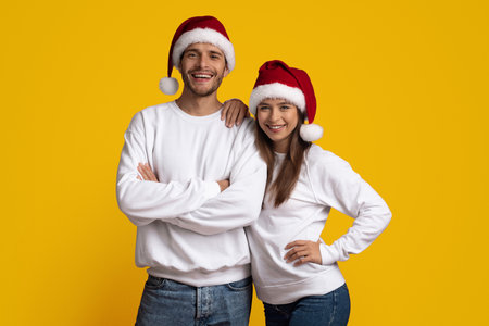 Smiling Couple in Christmas Hats Poses Against a Bright Yellow Background for Festive Celebrationの写真素材