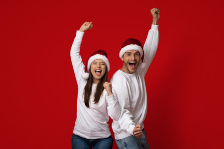 Joyful Young Couple Celebrating Christmas With Festive Hats Against a Vibrant Red Background