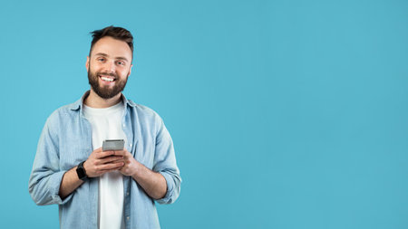 Man With a Beard Smiles While Using a Smartphone Against a Blue Background