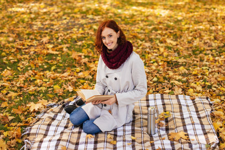Reading a Book on a Blanket Surrounded by Autumn Leaves in a Peaceful Outdoor Setting