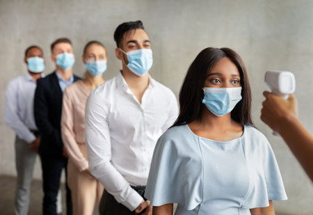 Group of Workers Undergoing Temperature Checks for Health Safety at Office Entrance
