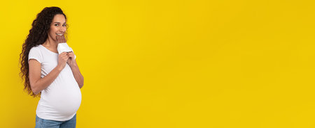 Pregnant Woman Happily Holding Against a Bright Yellow Backgroundの写真素材