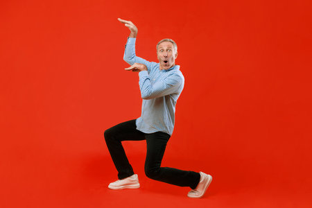 Man Posing With Excitement in Front of a Bright Red Background During a Fun Activityの写真素材