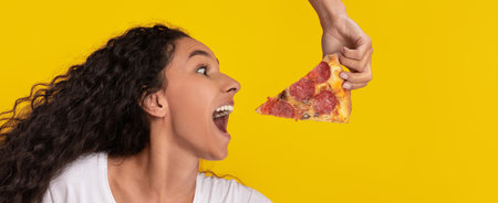 Woman Enjoys Pizza Slice Held by a Hand Against a Bright Yellow Backgroundの写真素材