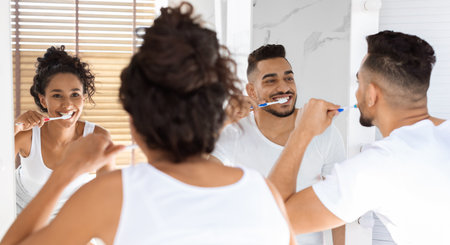 Couple Enjoying Morning Routine While Brushing Teeth in Bright Bathroom With Wooden Blindsの写真素材