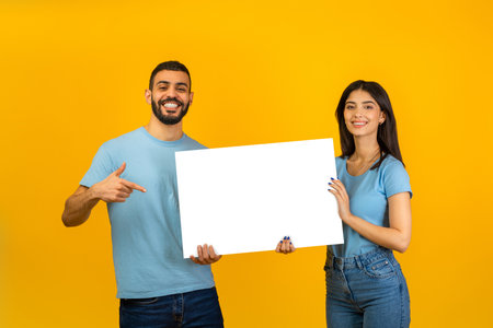 Happy Arab Couple Holding Blank Placard for Advertising With Bright Yellow Background