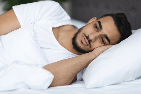 Upset Arab Man Lying in Bed, Struggling With Insomnia During Nighttimeの写真素材