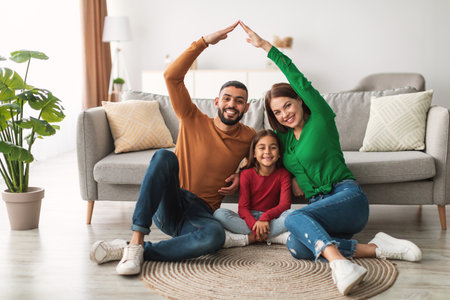 Happy Family Creating a Shelter of Hands Over Their Smiling Daughter at Homeの写真素材