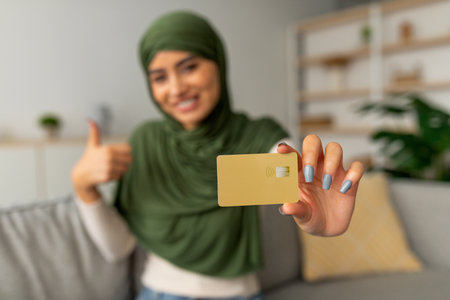 Young Arab Woman Shows off Credit Card With a Thumbs up Gesture at Homeの写真素材