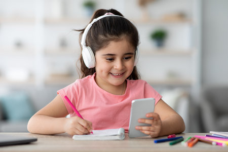 Young Girl Learning and Having Fun While Using a Smartphone at Home With Headphones On
