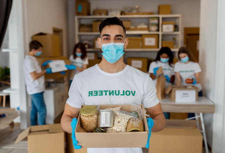 Male Volunteer at Charity Center Holds Food Donation Box With Friends Working in Background