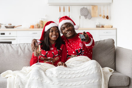 Happy Black Couple Celebrates Winter Holidays at Home While Watching TV and Enjoying Champagneの写真素材