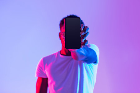 Young Man Displays Smartphone With Empty Screen for Mockup in Vibrant Neon Light Settingの写真素材