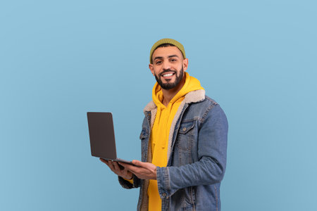 Smiling Man With a Laptop in a Casual Outfit Against a Blue Background