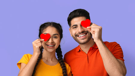 Young Couple Smiling and Holding Red Hearts in Front of a Purple Background