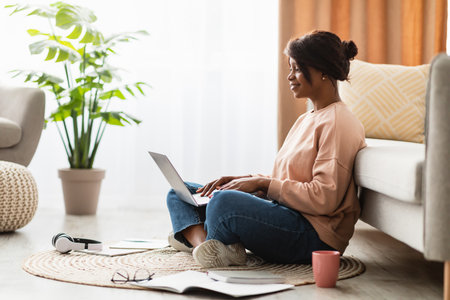 Woman Sitting on the Floor Using Laptop With Plants and Cozy Atmosphere in Modern Living Room During Daytimeの写真素材