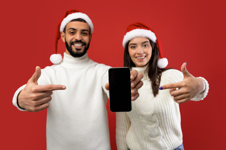 Happy Arab Couple Celebrating Christmas Together With Smartphone Over Red Backgroundの写真素材