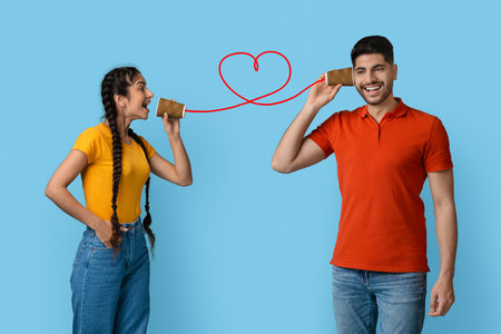 Couple Communicating Through Tin Can Phones With a Heart Shape Formed by the String on a Blue Backgroundの写真素材