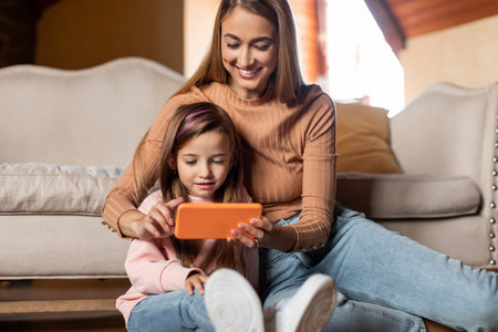 Mother and Daughter Enjoying Screen Time Together in Cozy Living Room Environment During Afternoon...