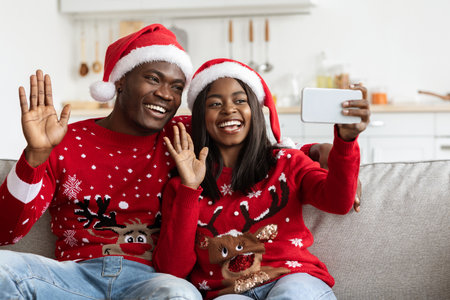 Happy Black Couple in Santa Hats Enjoying a Video Call While Celebrating Christmas at Homeの写真素材
