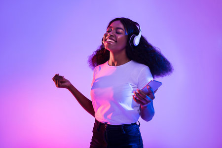 Happy African American Woman Enjoying Music and Dancing in Neon Light at Homeの写真素材