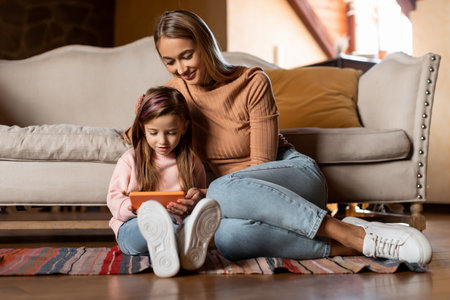 Mother and Daughter Enjoy Quality Time Together While Watching a Video on a Tablet in a Cozy Living Roomの写真素材