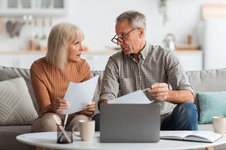 Elderly Couple Discussing Important Documents While Working Together at Home in a Cozy Living Room Settingの写真素材
