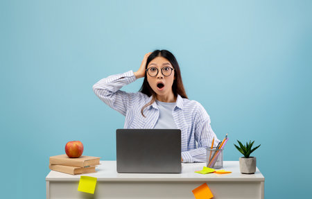 Woman Shocked While Working at Desk With Laptop, Books, and Plant, Against a Blue Background
