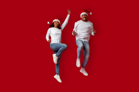 Joyful Couple Celebrating Christmas in Festive Hats and Cozy Outfits Against a Bright Red Backgroundの写真素材