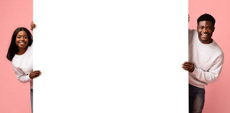 Stylish Young Black Man and Woman Happily Posing by Large Empty Advertising Boardの写真素材