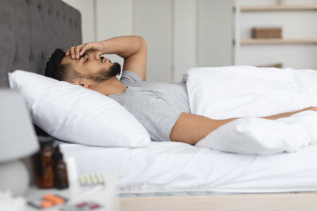 Sick Arab Man Resting in Bed With Medicine Nearby, Feeling Unwell at Homeの写真素材