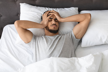 Young Arab Man Wakes up in Bed Feeling Headache and Stress After a Restless Nightの写真素材