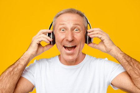 Older Man Enjoys Music While Wearing Headphones in Studio With a Bright Yellow Background