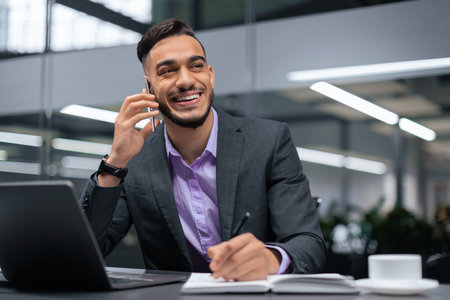 Businessman Talks on Phone While Taking Notes in Modern Office Settingの写真素材