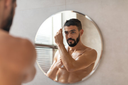 Guy Looking in Mirror Brushing Hair During Morning Preparation Routineの写真素材