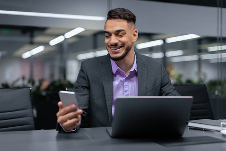 Man in Suit Looking at Smartphone While Sitting at Desk in Office During Daytime