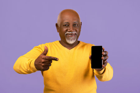 Man Points at Smartphone While Wearing a Yellow Sweater in Front of a Purple Background