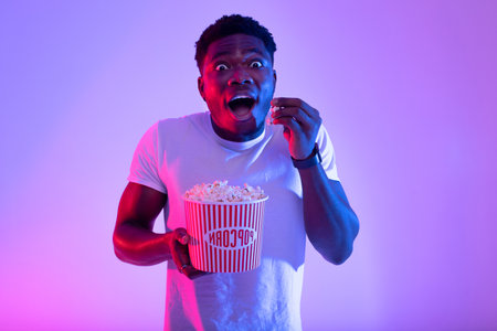 Excited Young Man Enjoying Popcorn While Watching a Movie in Vibrant Neon Lightsの写真素材