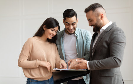 Three young adults reviewing documents together in a bright roomの写真素材