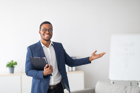 Friendly young African American psychologist with clipboard showing something with his hand at mental health clinicの写真素材