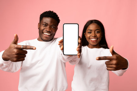 Cheerful Young African American Couple Shows Smartphone Mockup on Pink Backgroundの写真素材