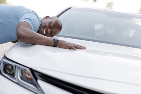 Ecstatic black man leaning on luxury car of his dreamの写真素材