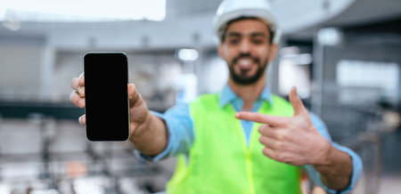 Worker Shows Smartphone in Construction Site While Wearing Safety Gear During Daylight Hours
